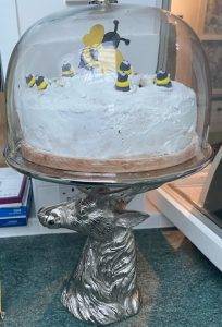 Pewter cake stand in the shape of a deer with an iced cake on top, decorated with sugar paste bees.