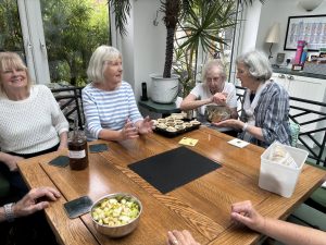 A group of visually impaired people sat around a table with one lady moulding some pastry over a bowl.